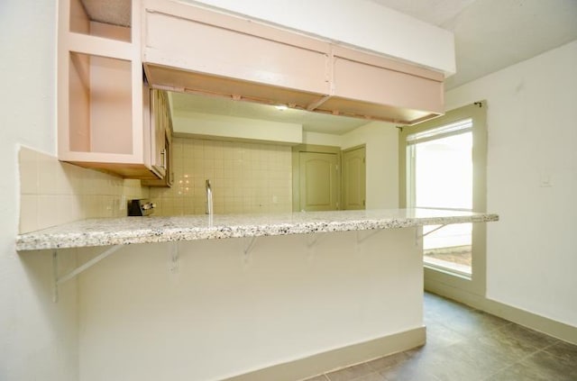 kitchen with tasteful backsplash, a kitchen breakfast bar, kitchen peninsula, and light stone countertops