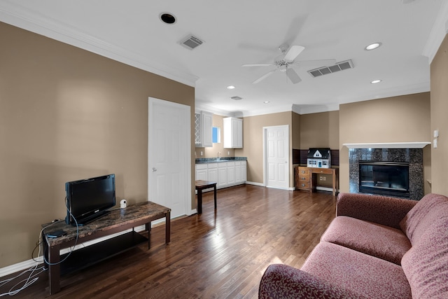 living room featuring sink, crown molding, dark wood-type flooring, ceiling fan, and a fireplace