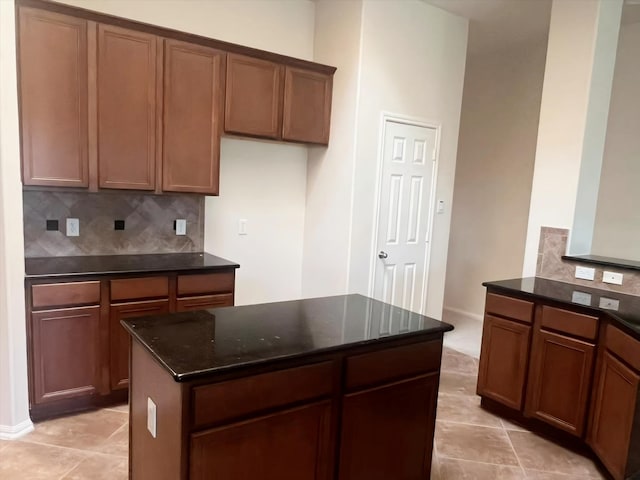 kitchen featuring light tile patterned flooring, dark stone counters, a kitchen island, and decorative backsplash