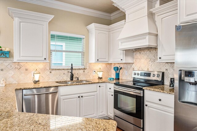 kitchen with sink, light stone counters, appliances with stainless steel finishes, custom range hood, and white cabinets