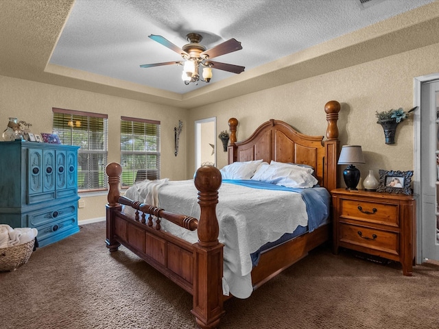 bedroom with ceiling fan, a tray ceiling, a textured ceiling, and dark colored carpet