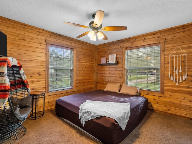 bedroom with ceiling fan, wooden walls, carpet floors, and a textured ceiling