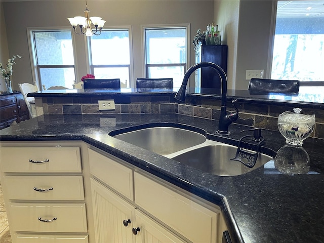 kitchen featuring sink, decorative light fixtures, a chandelier, dark stone counters, and white cabinets