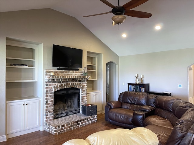 living room featuring vaulted ceiling, a brick fireplace, dark hardwood / wood-style floors, built in features, and ceiling fan