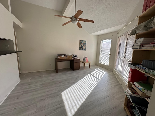 interior space with ceiling fan, high vaulted ceiling, a textured ceiling, and light wood-type flooring