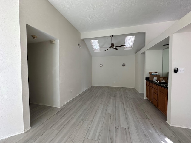 unfurnished living room with ceiling fan, vaulted ceiling with skylight, a textured ceiling, and light hardwood / wood-style flooring