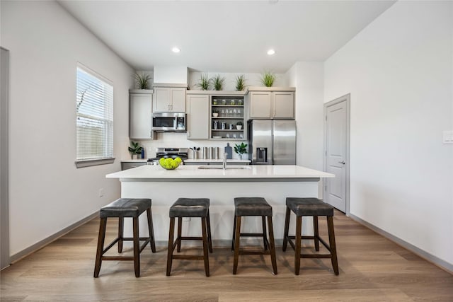 kitchen with appliances with stainless steel finishes, a kitchen breakfast bar, gray cabinets, and a center island with sink