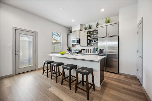 kitchen featuring stainless steel appliances, a kitchen bar, a kitchen island with sink, and gray cabinetry