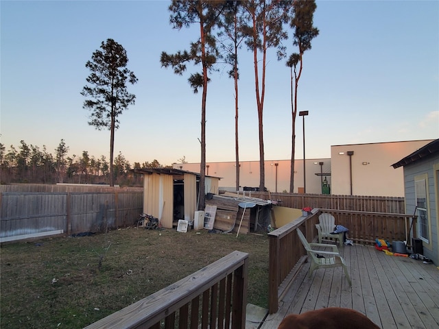 deck at dusk featuring a yard and a storage unit