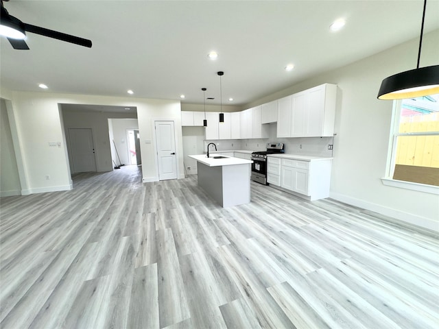 kitchen featuring sink, white cabinetry, decorative light fixtures, stainless steel stove, and a kitchen island with sink