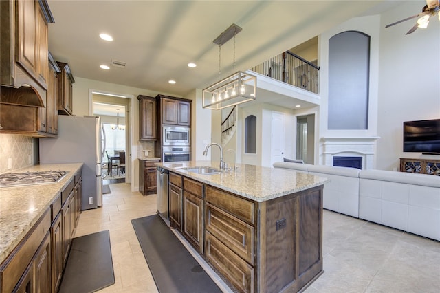 kitchen with sink, hanging light fixtures, stainless steel appliances, light stone countertops, and a center island with sink