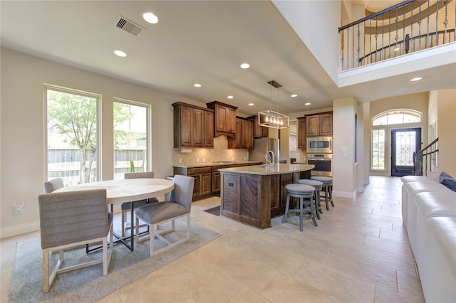 kitchen featuring pendant lighting, stainless steel appliances, an island with sink, a kitchen bar, and decorative backsplash