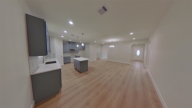 kitchen with gray cabinets, a kitchen island, decorative backsplash, hanging light fixtures, and light wood-type flooring