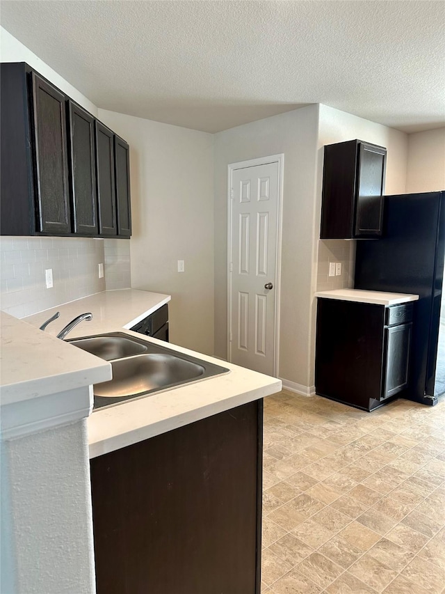 kitchen featuring tasteful backsplash, sink, black refrigerator, and a textured ceiling