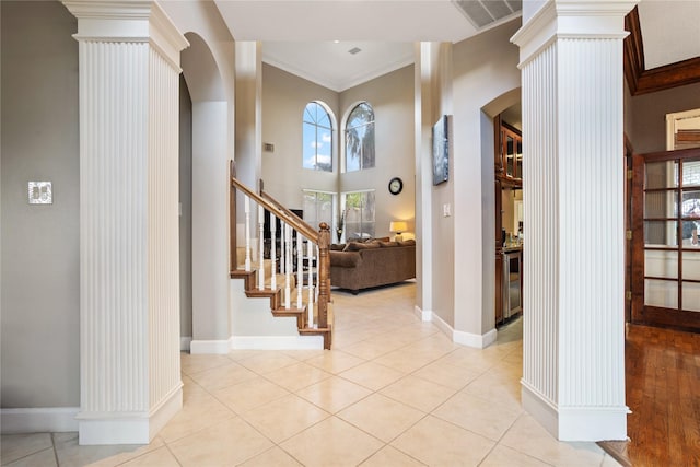 entrance foyer featuring ornamental molding, light tile patterned floors, a high ceiling, and ornate columns