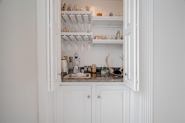 bar with sink, white cabinets, and dark stone counters