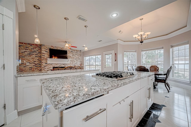 kitchen with stainless steel gas cooktop, a center island, hanging light fixtures, light stone countertops, and white cabinets