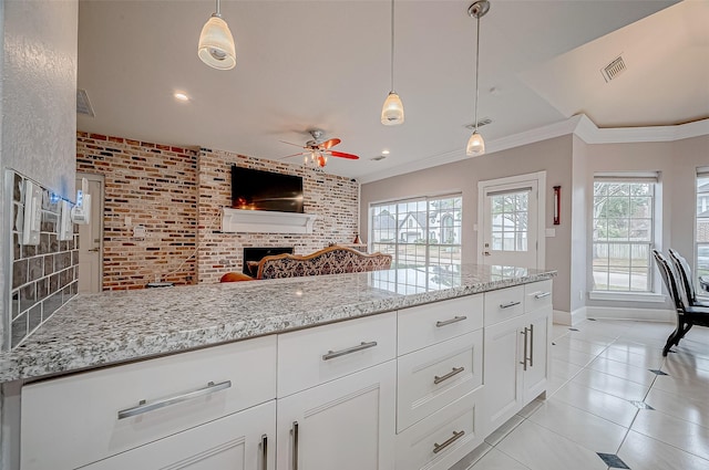 kitchen featuring brick wall, a fireplace, decorative light fixtures, white cabinetry, and ornamental molding