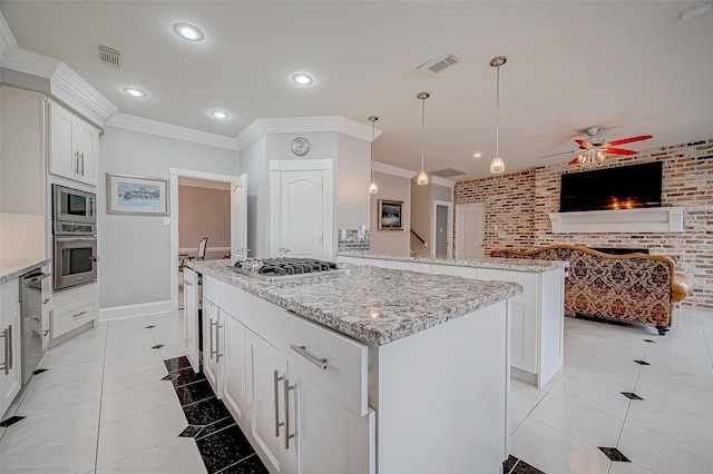 kitchen with appliances with stainless steel finishes, a kitchen island, pendant lighting, brick wall, and white cabinets