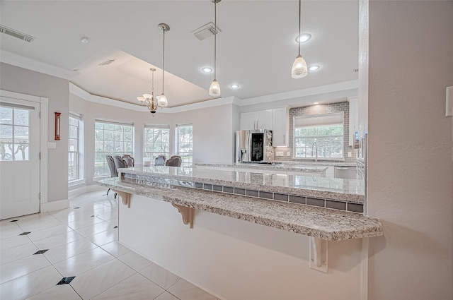 kitchen with crown molding, a breakfast bar, hanging light fixtures, white cabinets, and stainless steel fridge with ice dispenser