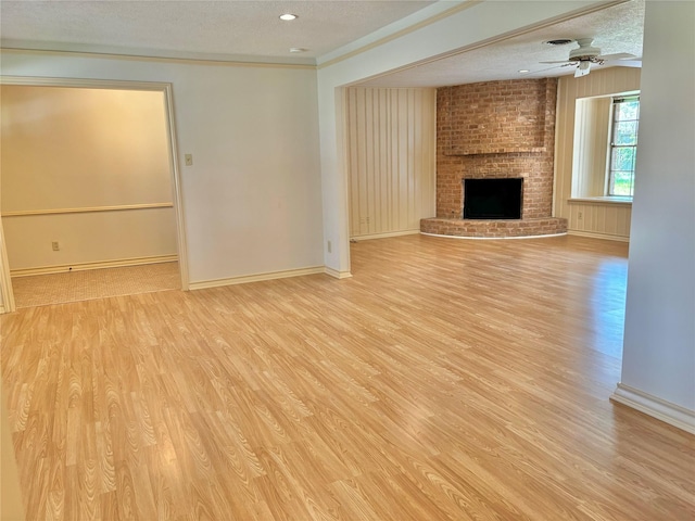 unfurnished living room with a brick fireplace, ceiling fan, a textured ceiling, and light wood-type flooring