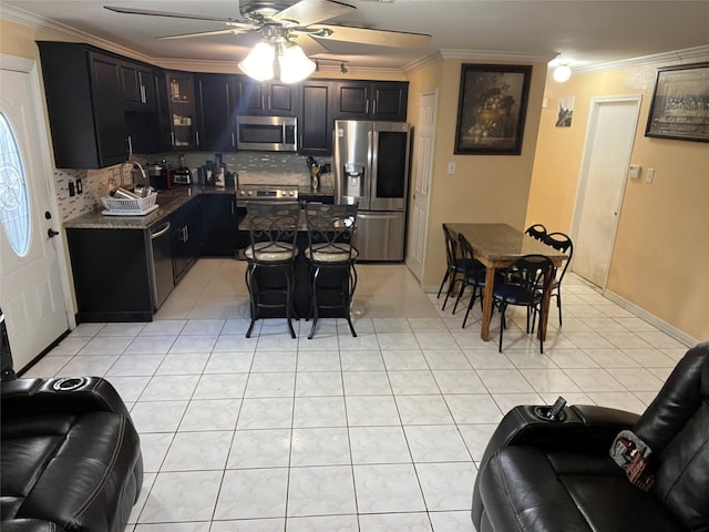 kitchen featuring light tile patterned flooring, a kitchen bar, crown molding, tasteful backsplash, and appliances with stainless steel finishes