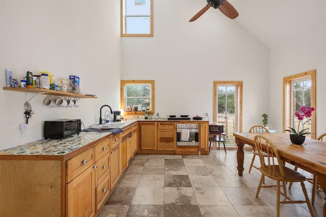 kitchen featuring high vaulted ceiling, sink, stainless steel oven, and ceiling fan