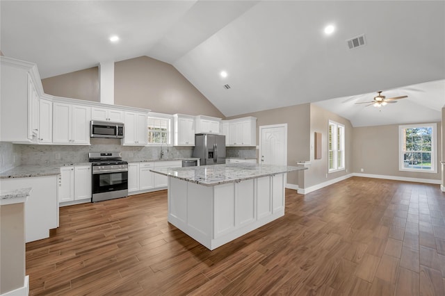 kitchen with appliances with stainless steel finishes, hardwood / wood-style floors, white cabinets, a center island, and light stone counters