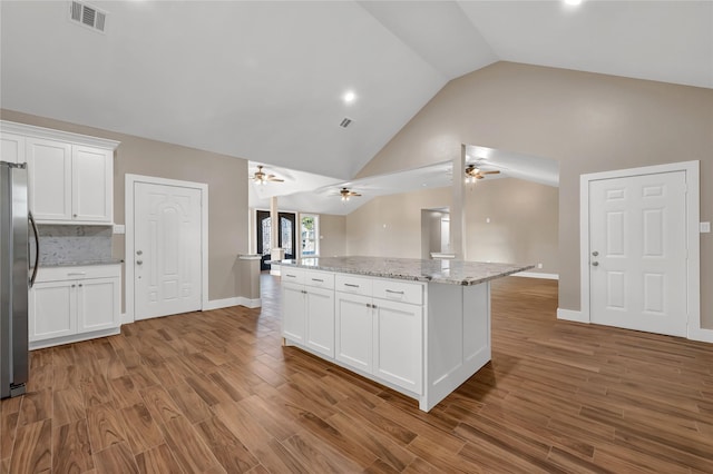 kitchen featuring stainless steel refrigerator, light stone countertops, a kitchen island, and white cabinets