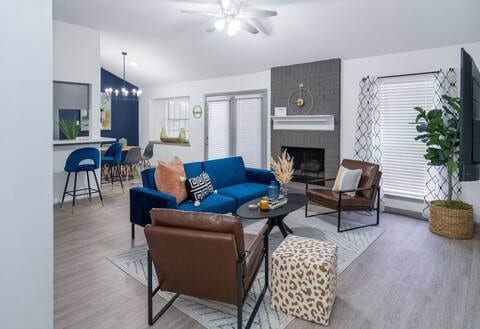 living room with a brick fireplace, hardwood / wood-style flooring, vaulted ceiling, and ceiling fan with notable chandelier