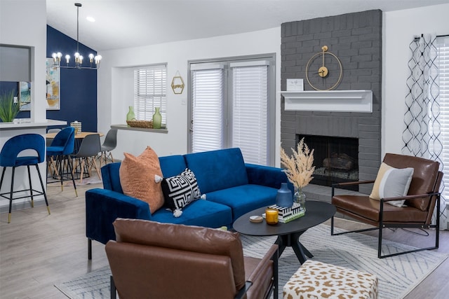 living room with lofted ceiling, a fireplace, light hardwood / wood-style flooring, and a notable chandelier