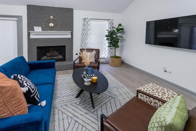 living room with vaulted ceiling, hardwood / wood-style floors, and a brick fireplace