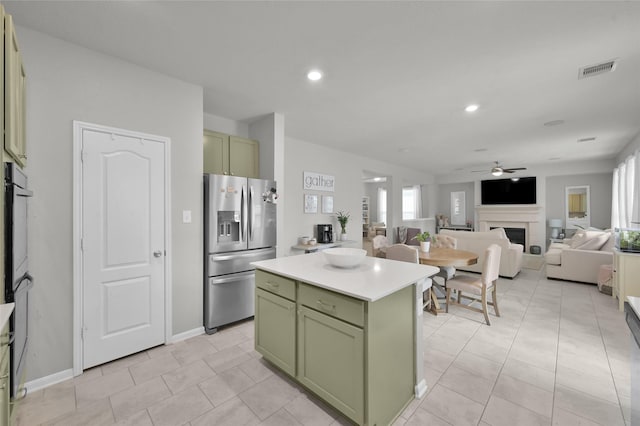 kitchen with light tile patterned floors, ceiling fan, green cabinets, stainless steel refrigerator with ice dispenser, and a kitchen island