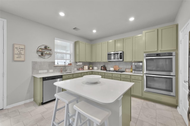 kitchen with sink, a breakfast bar area, green cabinets, stainless steel appliances, and tasteful backsplash