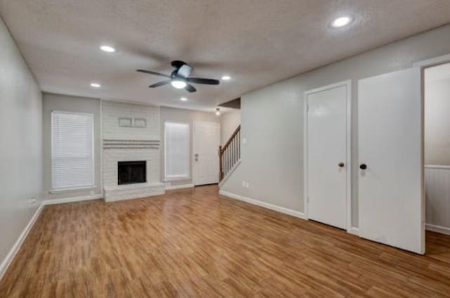 unfurnished living room with ceiling fan, hardwood / wood-style flooring, a fireplace, and a textured ceiling