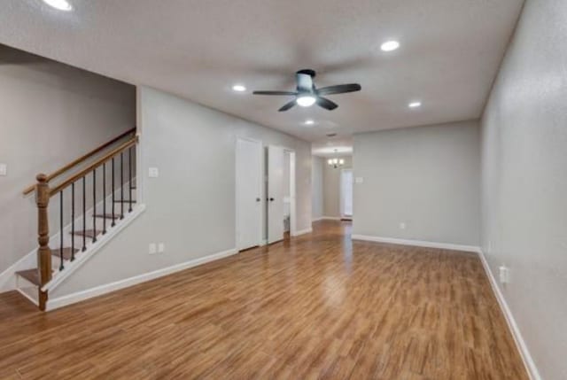 unfurnished living room featuring ceiling fan with notable chandelier and hardwood / wood-style floors