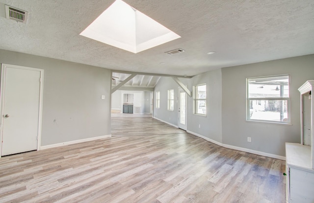 unfurnished living room featuring a skylight, light hardwood / wood-style floors, and a textured ceiling