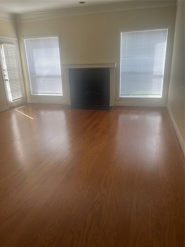 unfurnished living room featuring wood-type flooring, a wealth of natural light, and crown molding