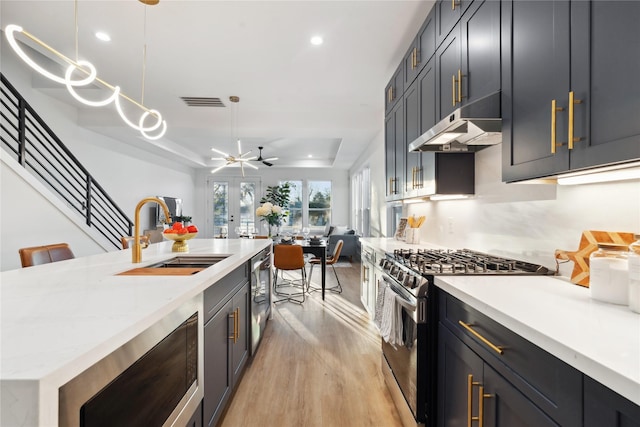 kitchen with sink, light stone counters, decorative light fixtures, light hardwood / wood-style flooring, and stainless steel appliances