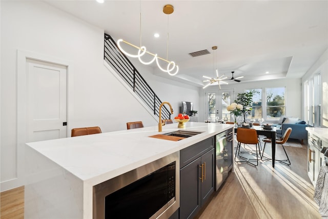 kitchen with pendant lighting, an island with sink, sink, a tray ceiling, and stainless steel appliances