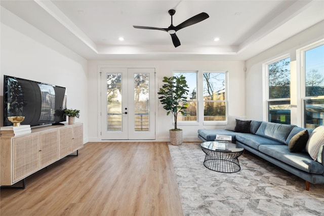 living room with french doors, ceiling fan, a tray ceiling, and light hardwood / wood-style floors