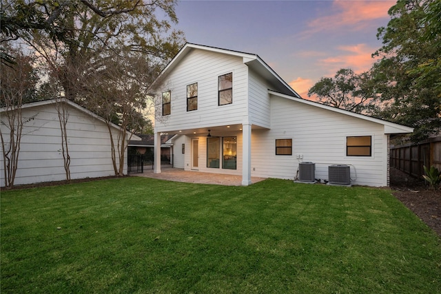 back house at dusk with a yard, a patio area, and central air condition unit