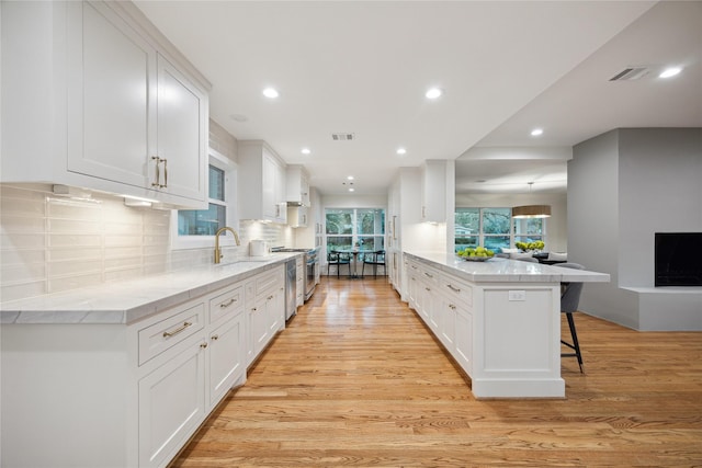 kitchen with high end stove, a kitchen breakfast bar, white cabinets, and light wood-type flooring