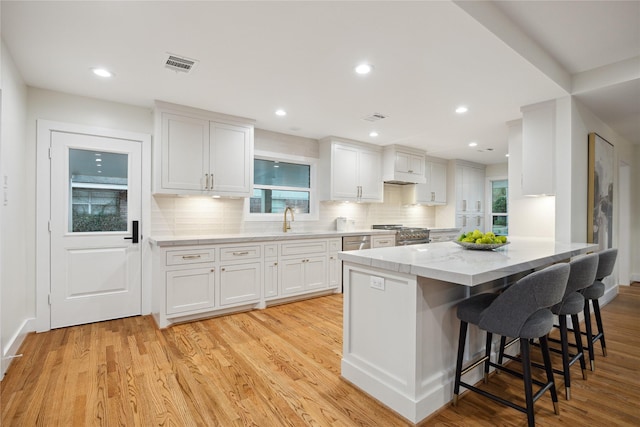 kitchen featuring sink, white cabinetry, a kitchen breakfast bar, high end stove, and light wood-type flooring