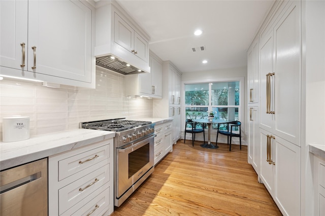 kitchen featuring light hardwood / wood-style flooring, appliances with stainless steel finishes, white cabinetry, light stone counters, and decorative backsplash