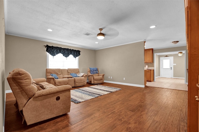 living room featuring ceiling fan, ornamental molding, a textured ceiling, and light hardwood / wood-style floors