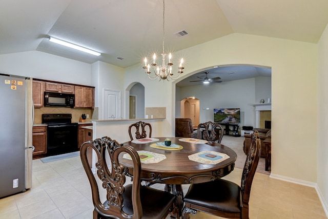 dining area with ceiling fan with notable chandelier, a tiled fireplace, vaulted ceiling, and light tile patterned floors