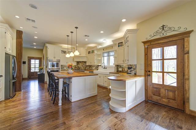 kitchen featuring wood counters, decorative light fixtures, stainless steel appliances, and white cabinets