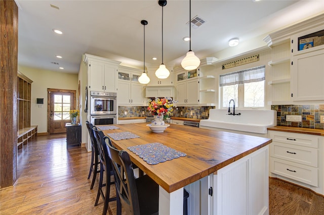 kitchen featuring pendant lighting, butcher block countertops, a center island, white cabinets, and stainless steel double oven