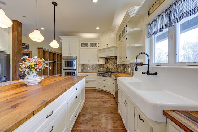 kitchen with hanging light fixtures, white cabinetry, appliances with stainless steel finishes, and butcher block counters